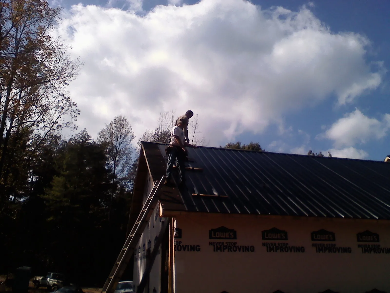 Roofer fastening dark metal panels high against a cloudy sky, from a Roof Inspection job in Collingswood